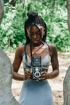 Woman holding vintage camera outdoors amidst natural surroundings.