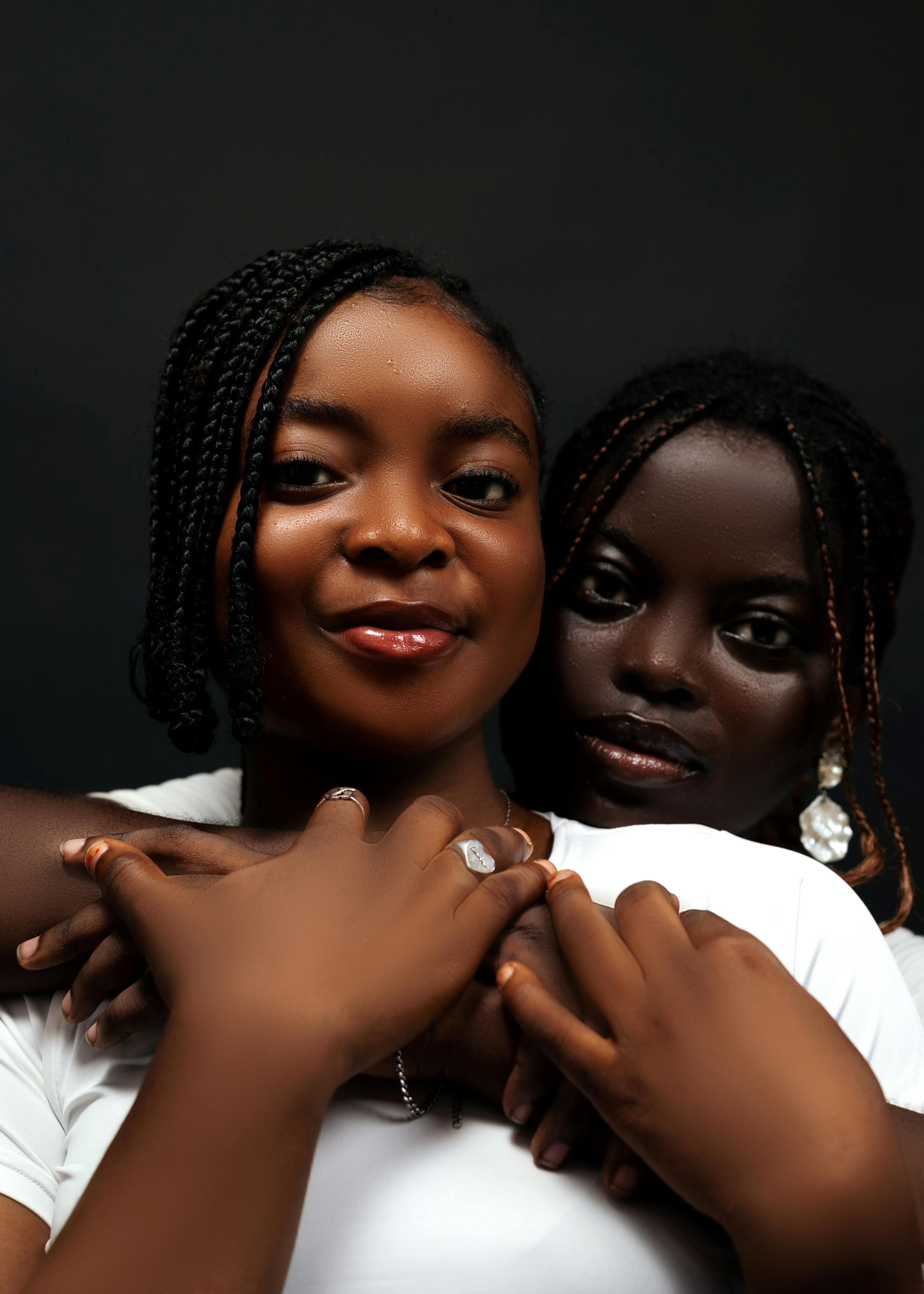 Close-up portrait of two young women embracing with a dark background.