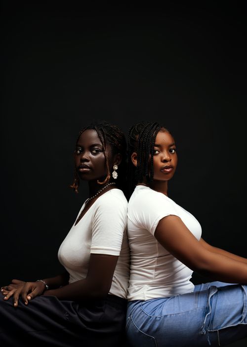 Free Artistic studio portrait of two young women sitting back to back in white tops, embracing individuality. Stock Photo