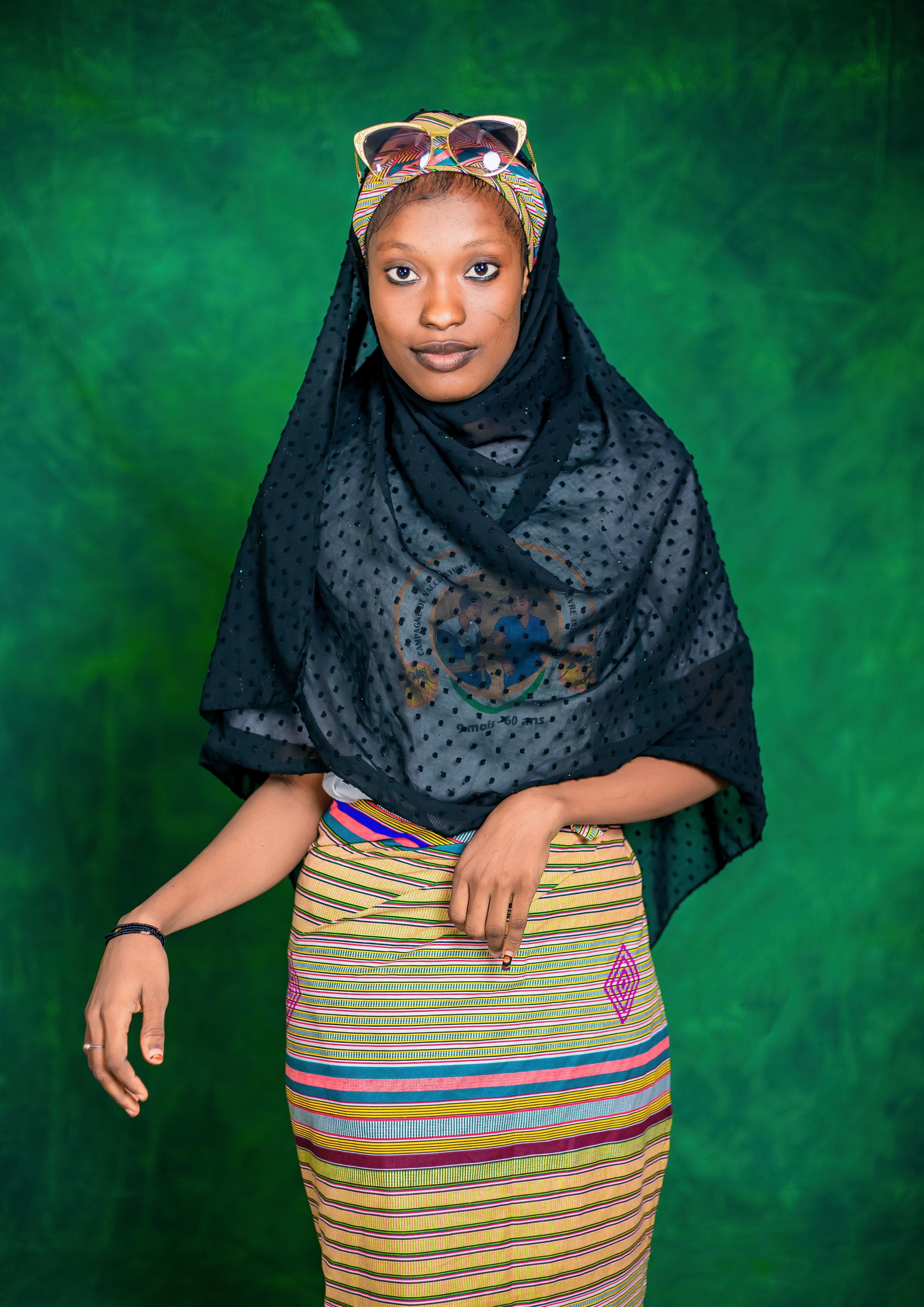Portrait of a young woman wearing colorful traditional African clothing against a green background.