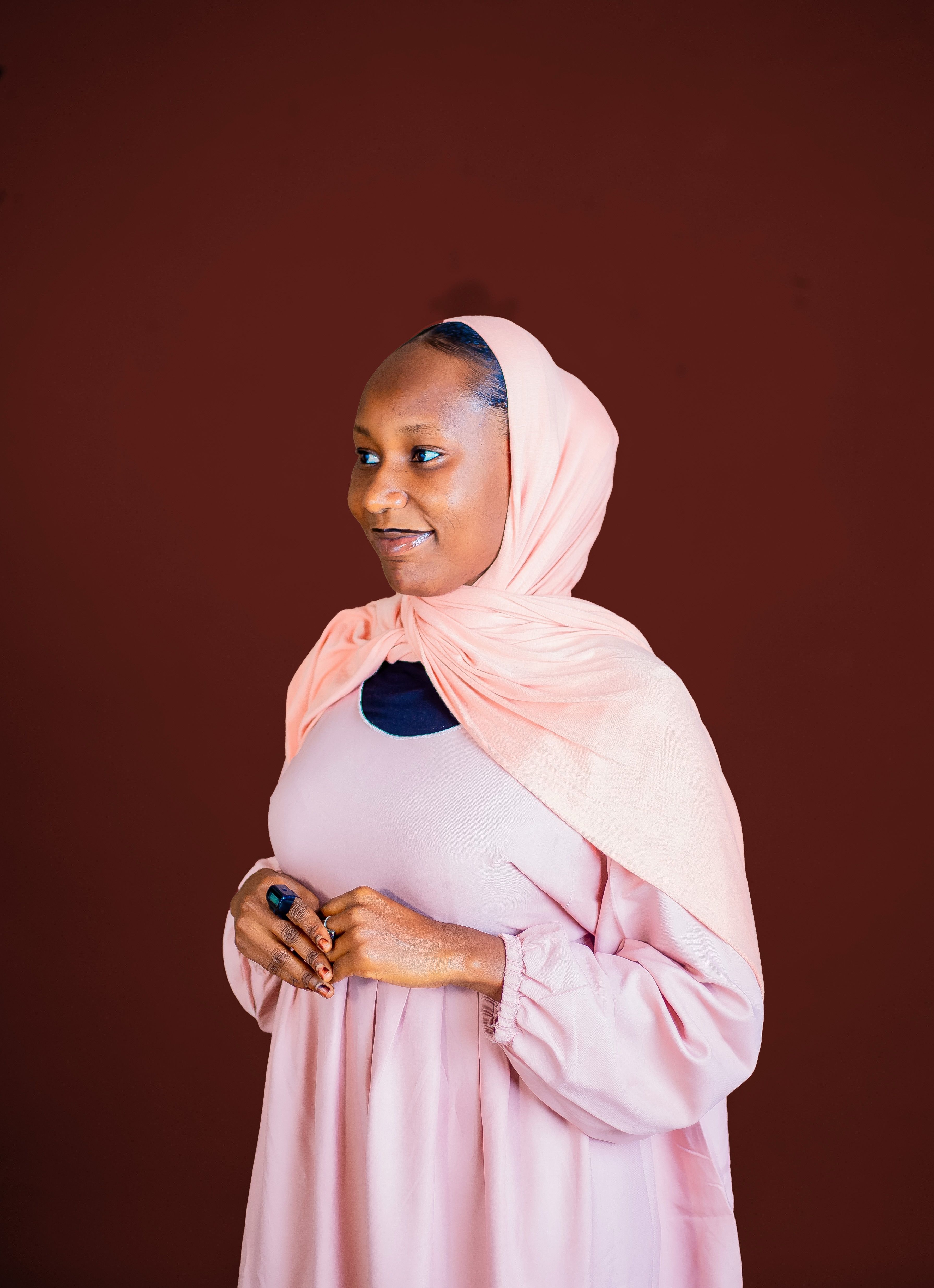 Elegant portrait of a smiling woman in a pink hijab against a warm brown backdrop.