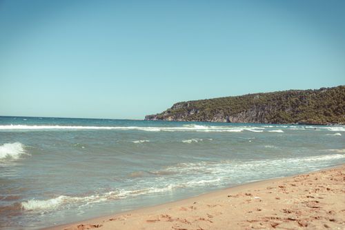 Free Tranquil beach scene with gentle waves and distant rocky shoreline under a clear sky. Stock Photo