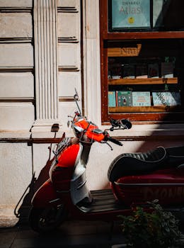 Red vintage scooter parked outside a bookstore with a sunlit facade, conveying a nostalgic urban scene.