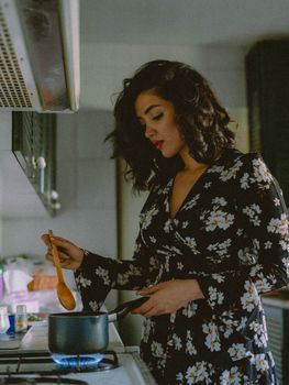 Woman stirring pot in kitchen, wearing floral dress. Warm, cozy atmosphere.