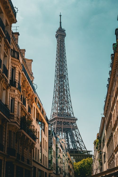 Free Iconic Eiffel Tower view from a Parisian street, highlighting classic French architecture under a clear sky. Stock Photo
