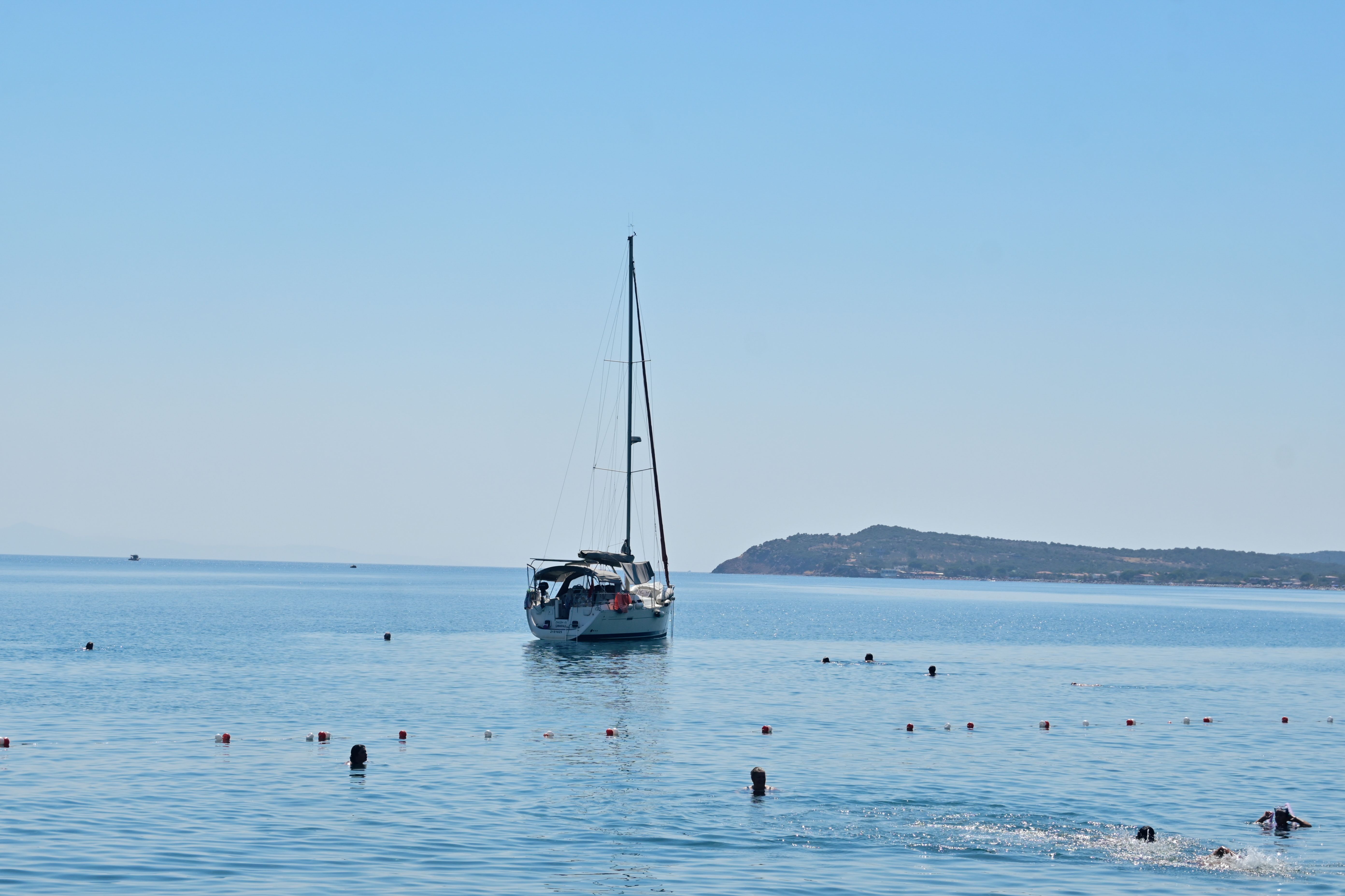 Sailing boat and swimmers enjoying a sunny day in Çanakkale, Türkiye.