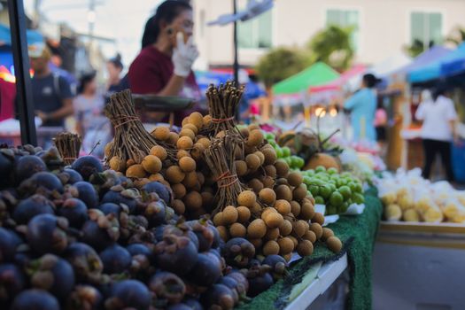 Bustling Thai market with fresh mangosteen and longan fruits on display.