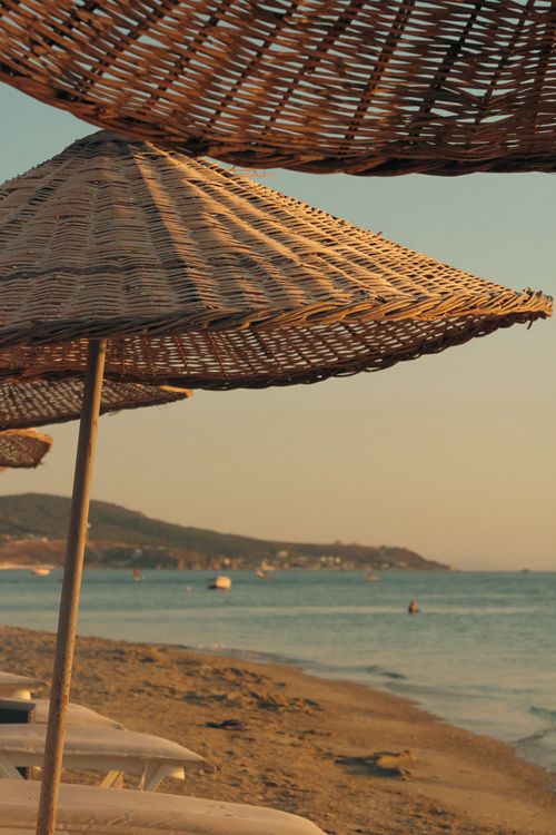Free Relaxing beach scene with straw umbrellas at sunset, capturing serene coastal vibes. Stock Photo