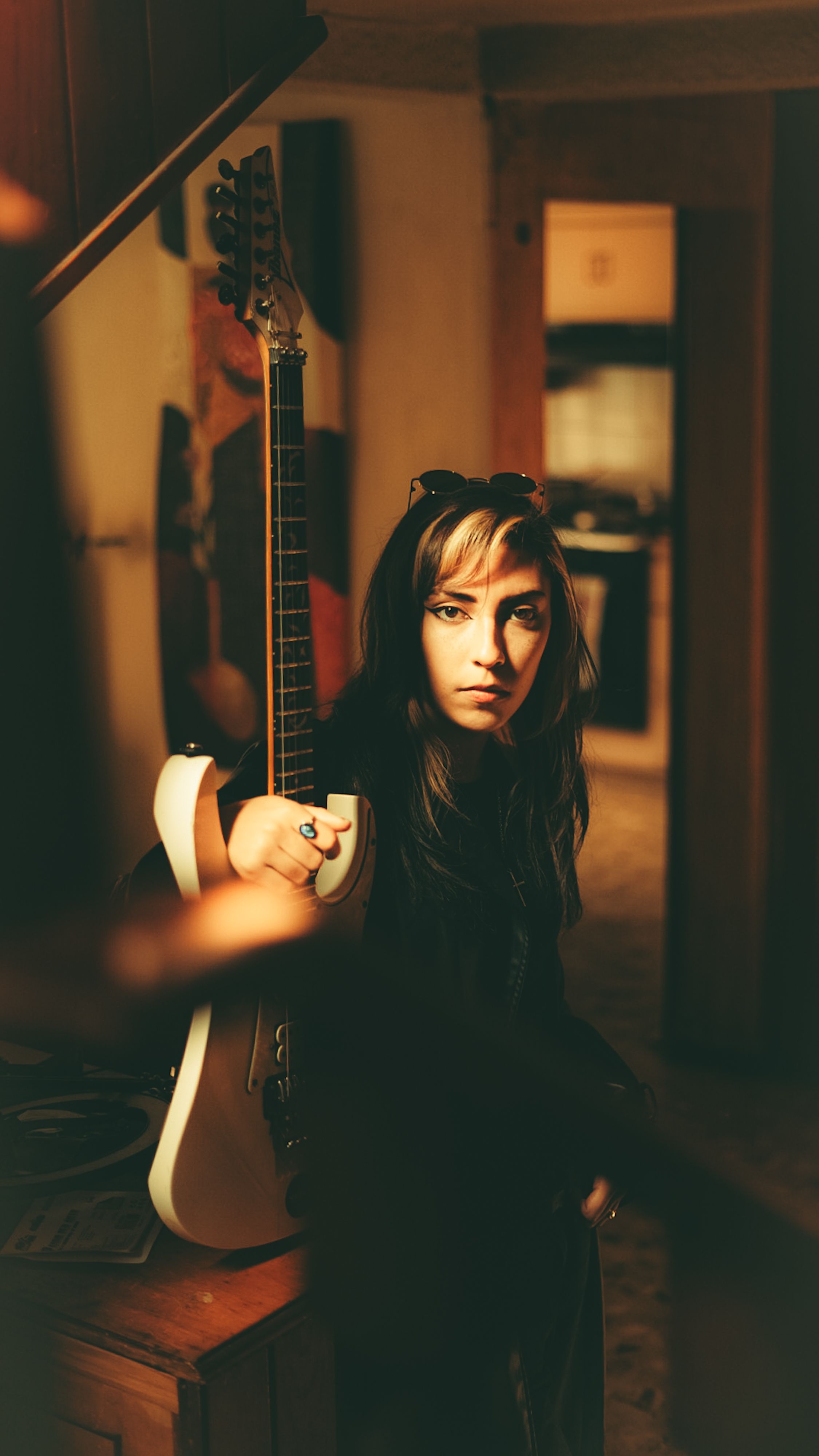 Fotomural Una mujer joven parada en el interior sosteniendo una guitarra y dando una mirada contemplativa.
