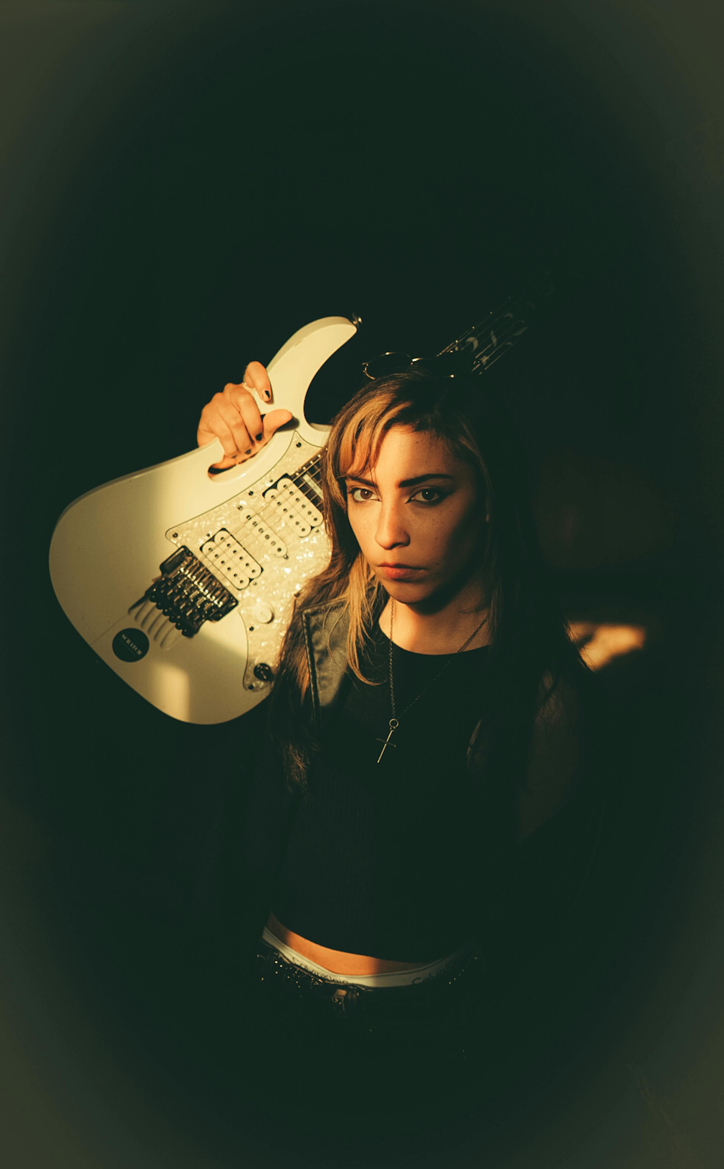 A woman with a white electric guitar, captured in warm, dramatic lighting, showcasing rock style.