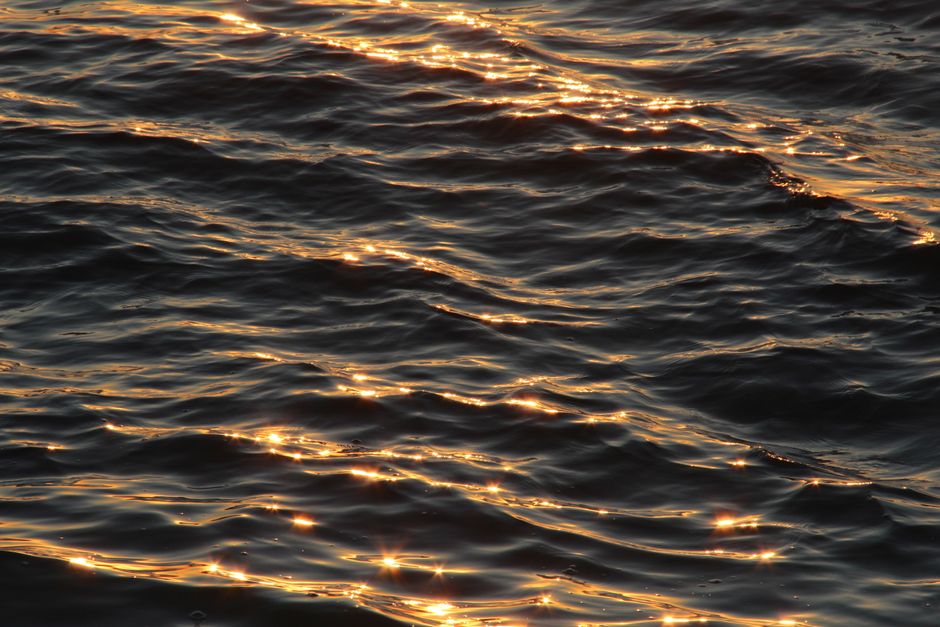 Close-up shot of golden sunlight reflecting off calm ocean waves during sunset, creating a serene and peaceful atmosphere.