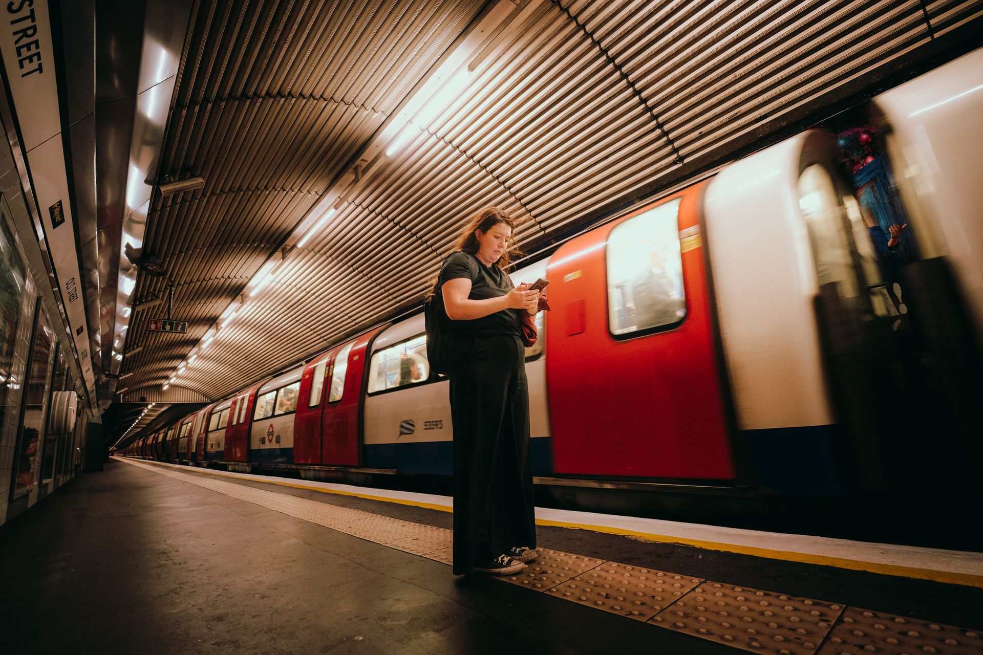 A woman uses her phone while waiting at a London Underground station as a train arrives.
