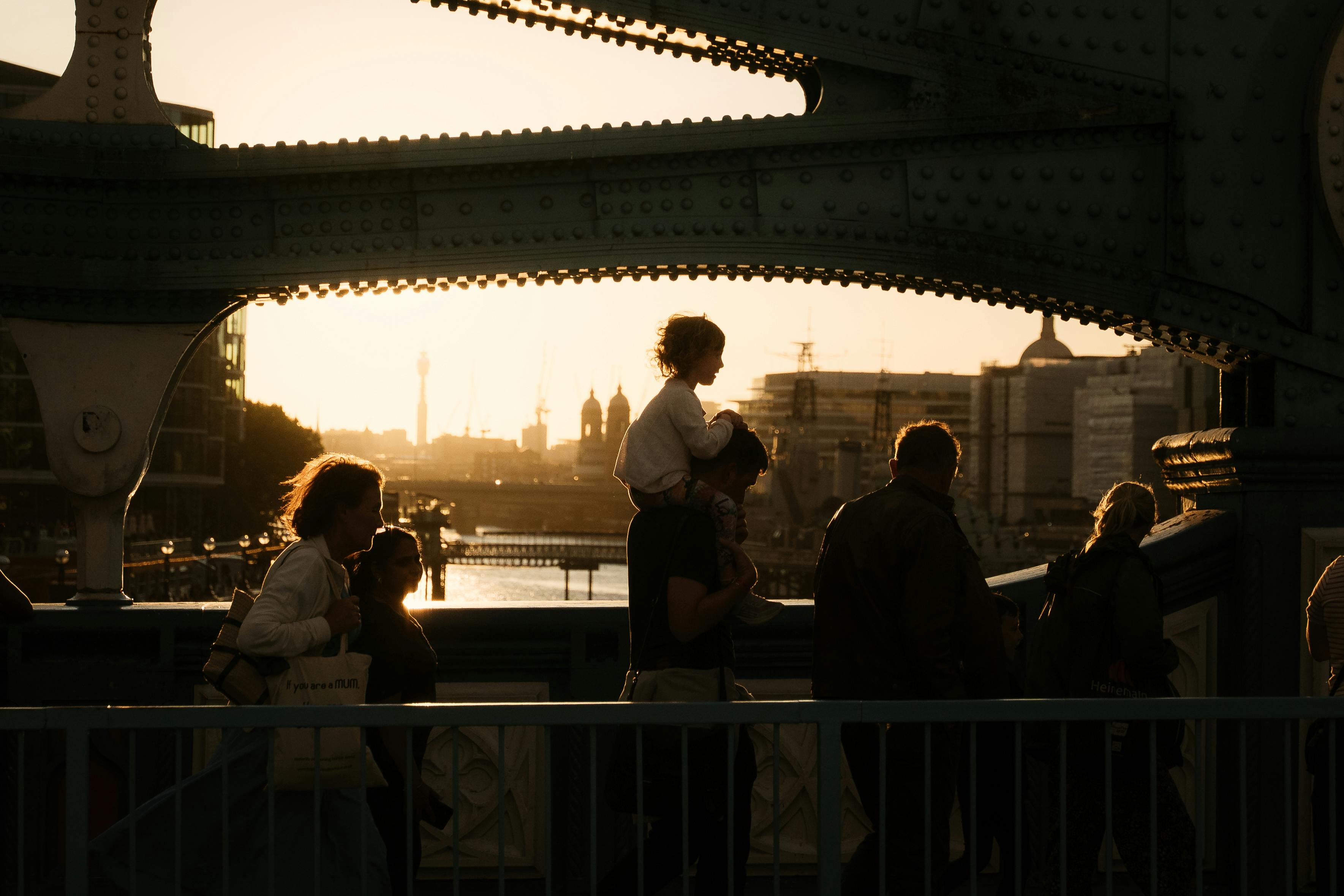Silhouetted people walking across Tower Bridge in London at sunset, highlighting the iconic skyline.