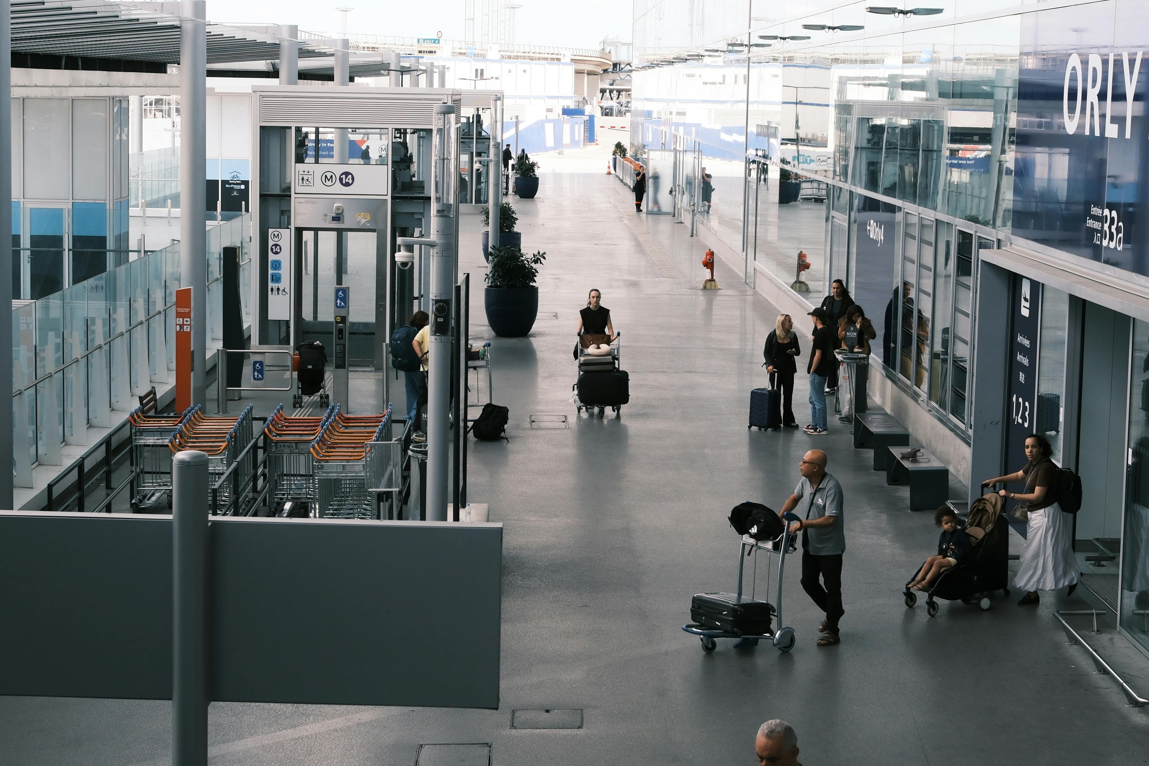 Travelers move through an airport terminal with luggage carts and suitcases.