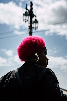 Vibrant portrait of a woman with pink hair wearing a denim jacket in Brighton. Captured outdoors under a blue sky.
