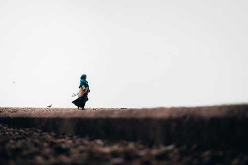 Free A woman in a blue hijab walks alone along Brighton Beach, surrounded by seagulls. Stock Photo