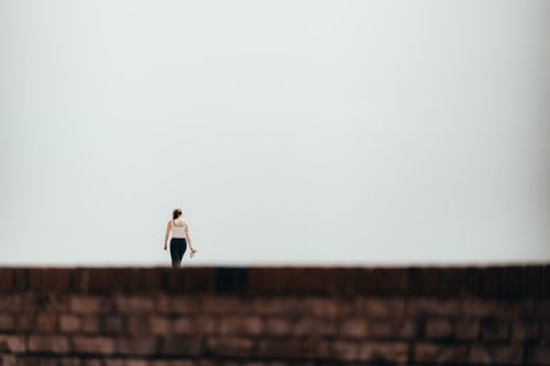 Free A solitary woman walks on a pier against a vast clear sky in Brighton, UK. Stock Photo