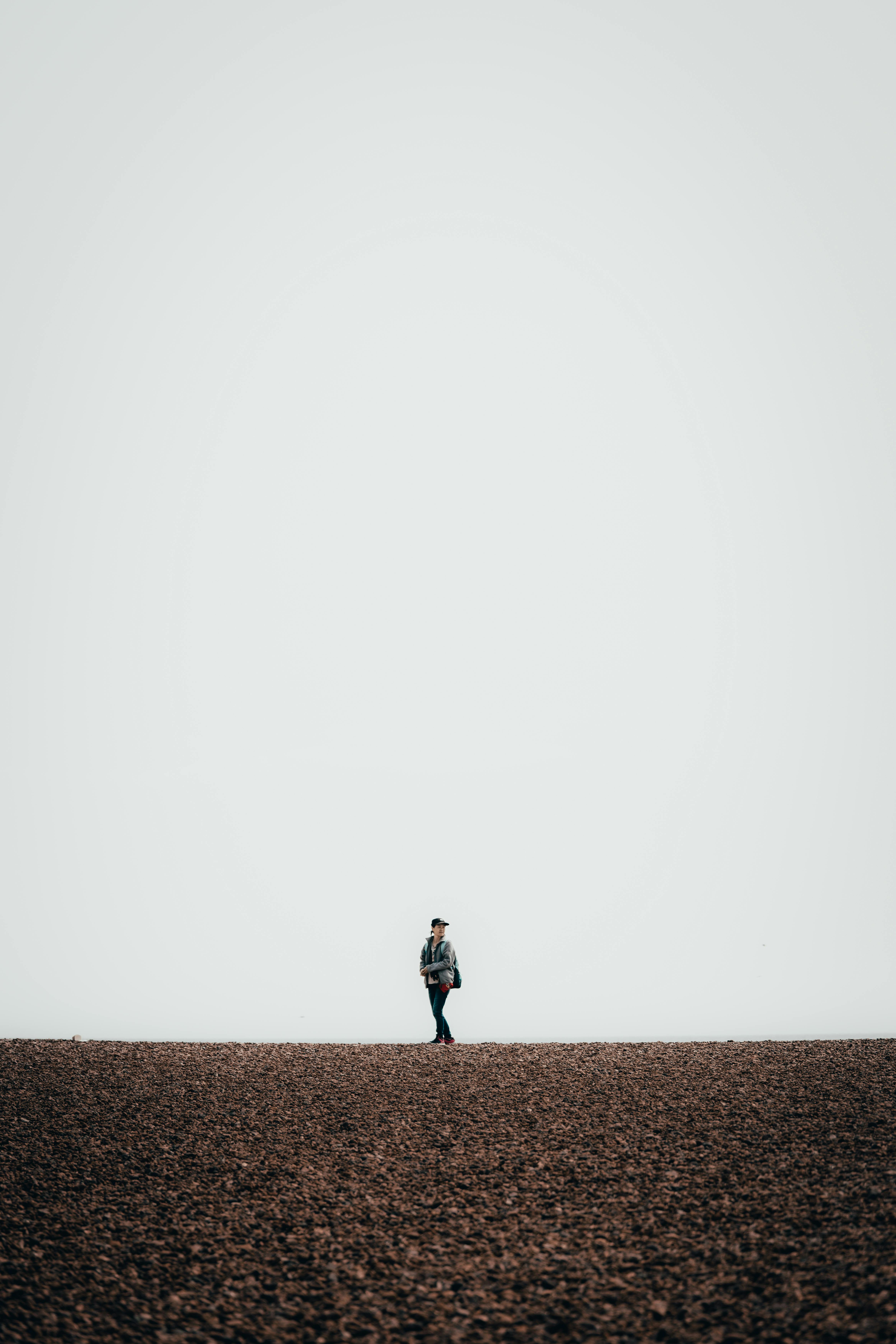 Minimalist photo of a person walking alone on Brighton's pebble beach under a vast sky.