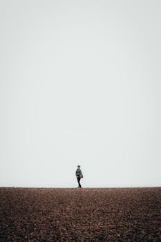 Minimalist photo of a person walking alone on Brighton's pebble beach under a vast sky.