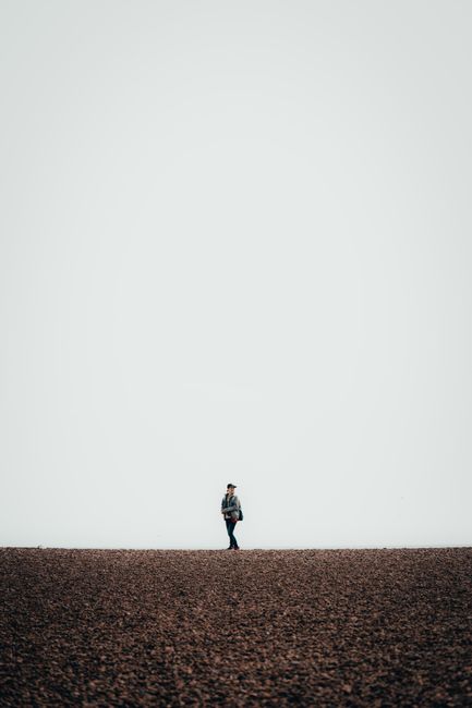 Minimalist photo of a person walking alone on Brighton's pebble beach under a vast sky.