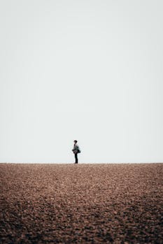 A solitary figure stands on a wide pebble beach at Hove, England, under an expansive sky.