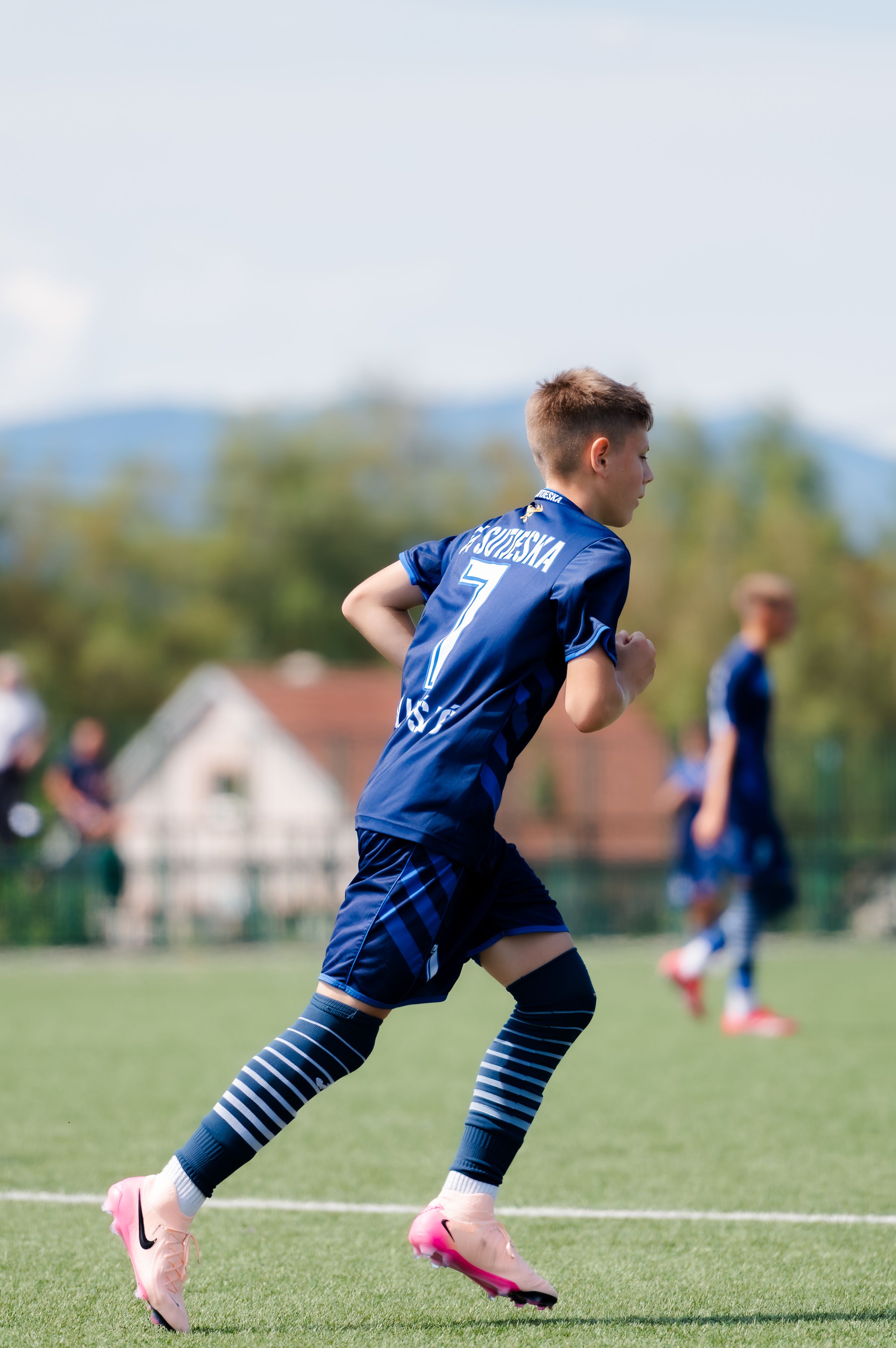 Boy in blue soccer uniform running during a game on a clear day.