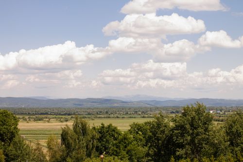 Free A serene rural landscape featuring lush fields, distant mountains, and a clear blue sky with scattered clouds. Stock Photo