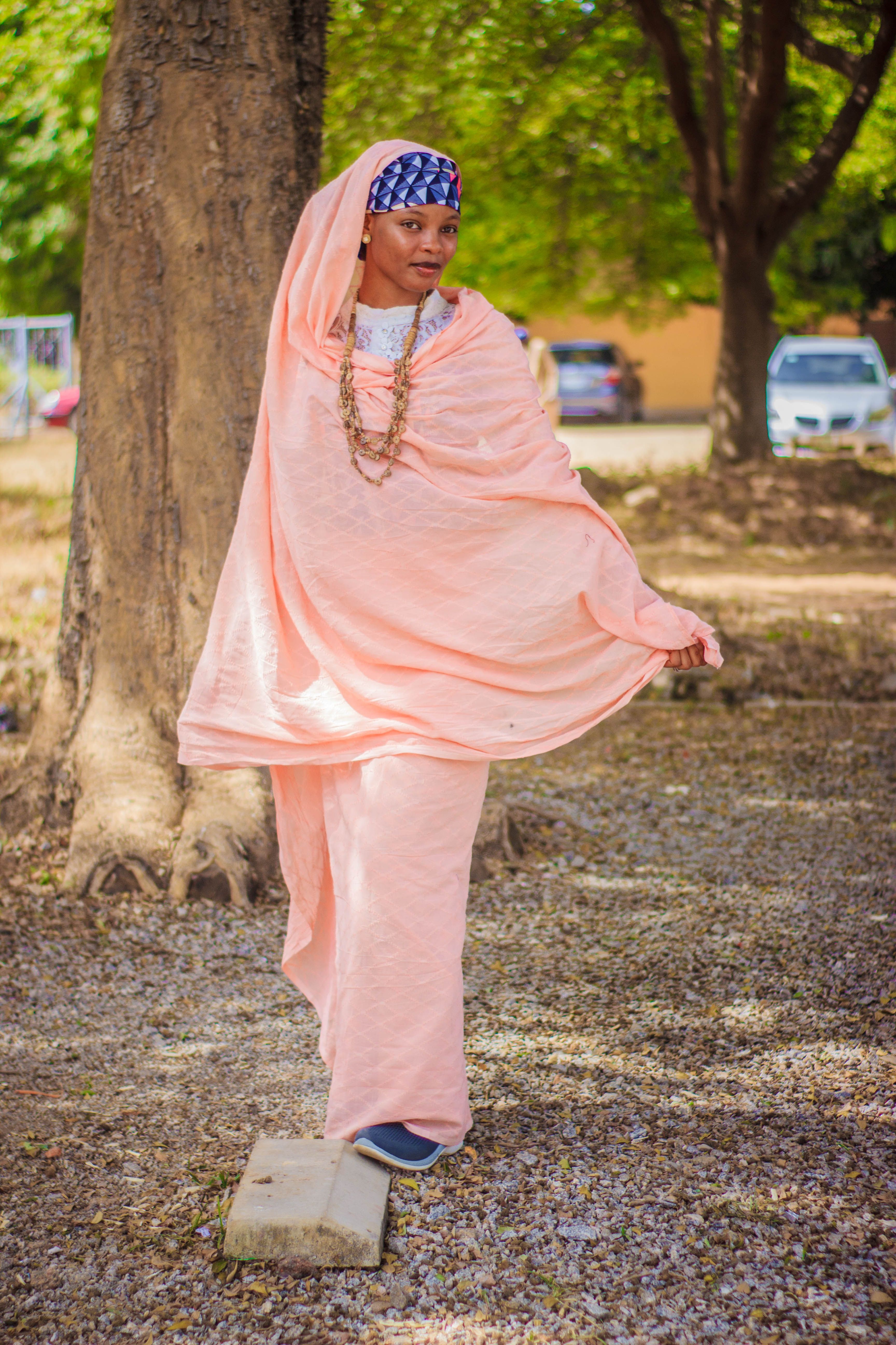 Woman in traditional pink attire posing outdoors by a tree.