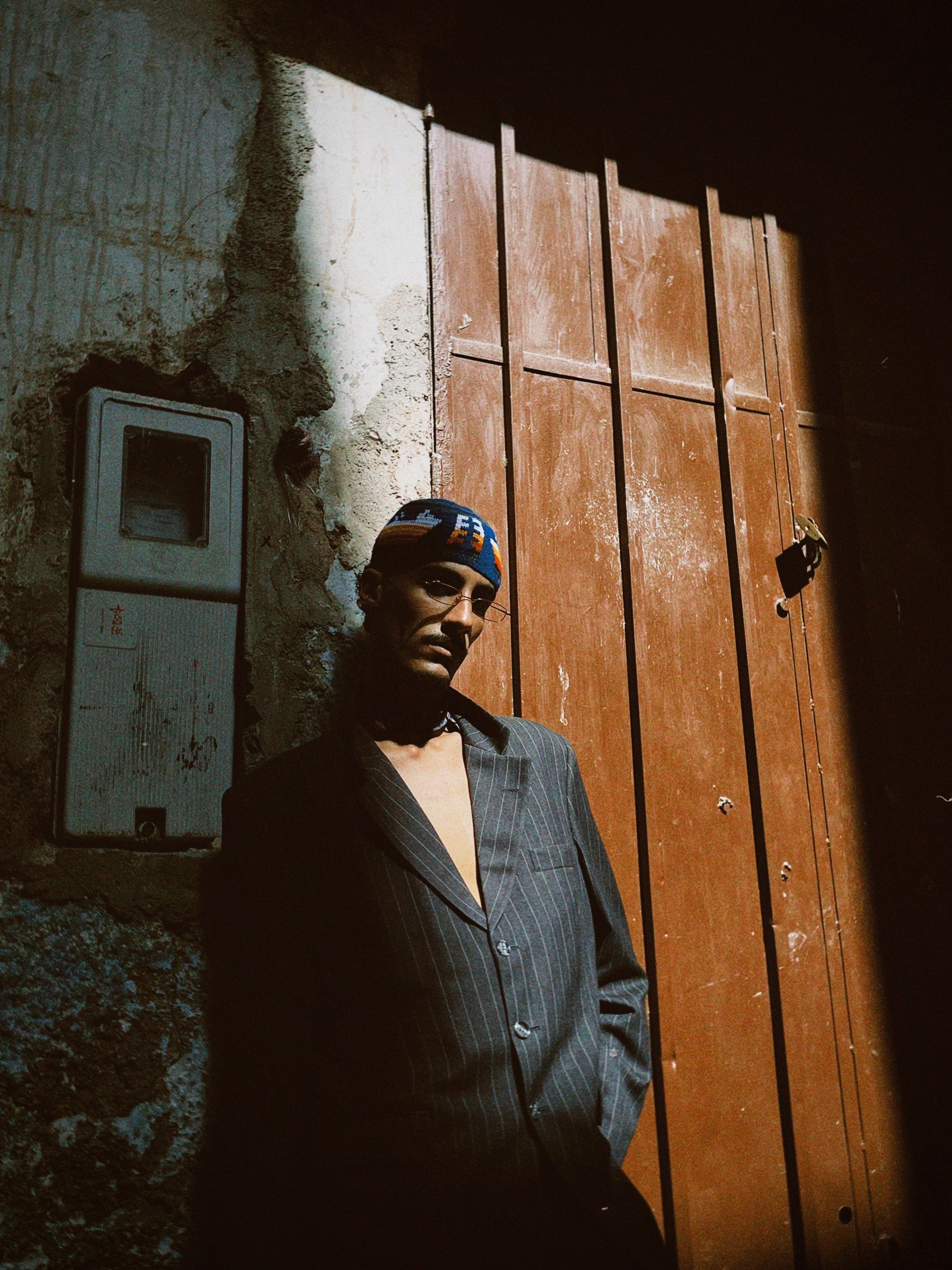 Moody portrait of a man in an alleyway, illuminated by sunlight with dramatic shadows.