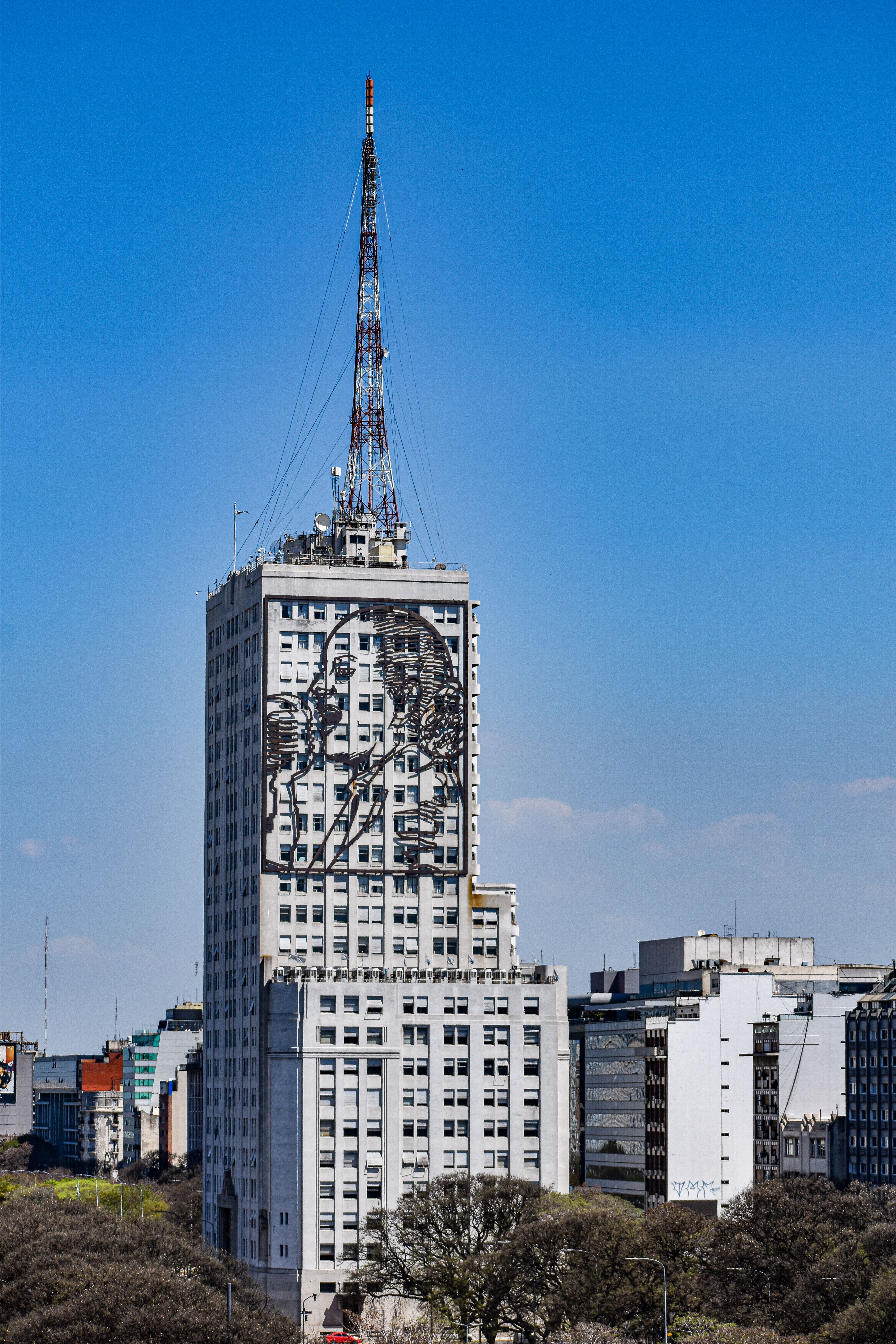 Skyscraper in Buenos Aires with Evita Perón artwork and antenna against blue sky.