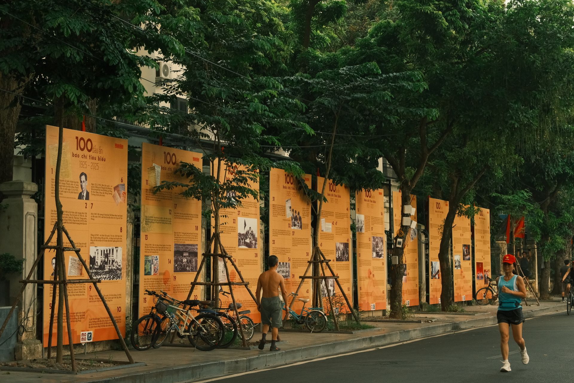 Two people jogging along a street lined with orange exhibition panels under green trees.