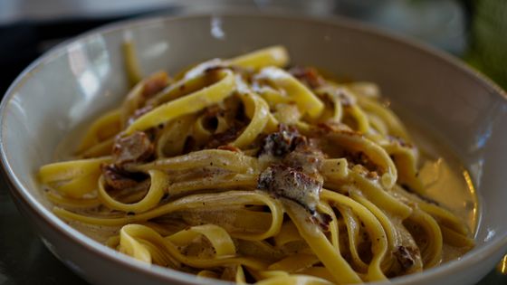 Tagliatelle in a light buttery sauce with sauteed dark mushrooms in a pale bowl