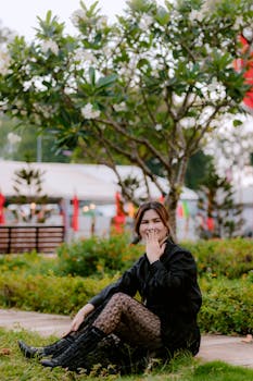 Woman in a black outfit enjoying a serene garden setting with greenery and trees.