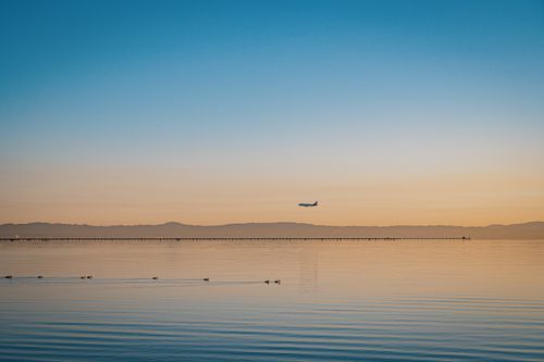 Free A serene view of an airplane flying over calm ocean waters at sunset, with warm tones and peaceful ambiance. Stock Photo