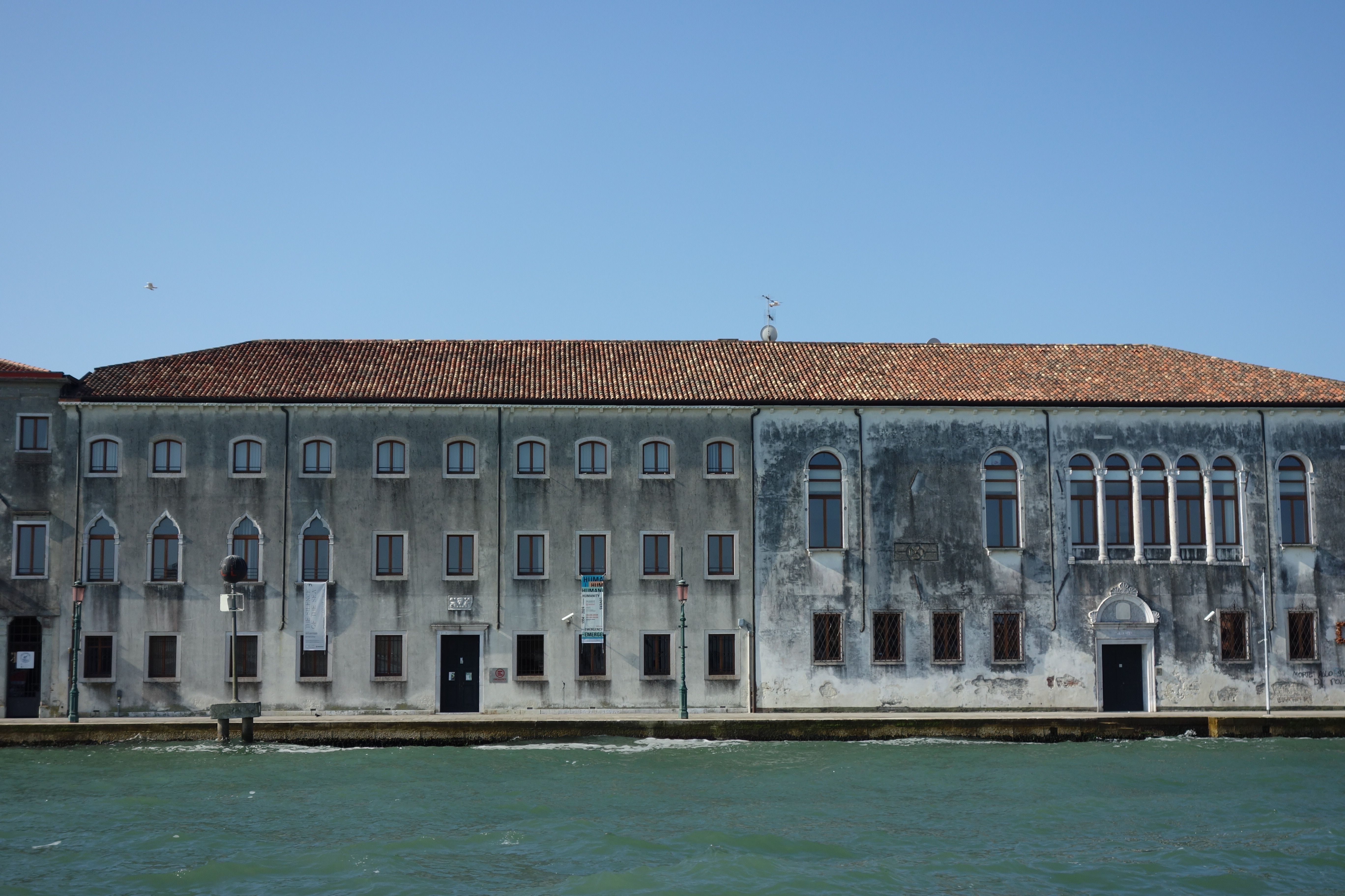 Old Venetian building with arched windows by the waterfront under clear blue sky.