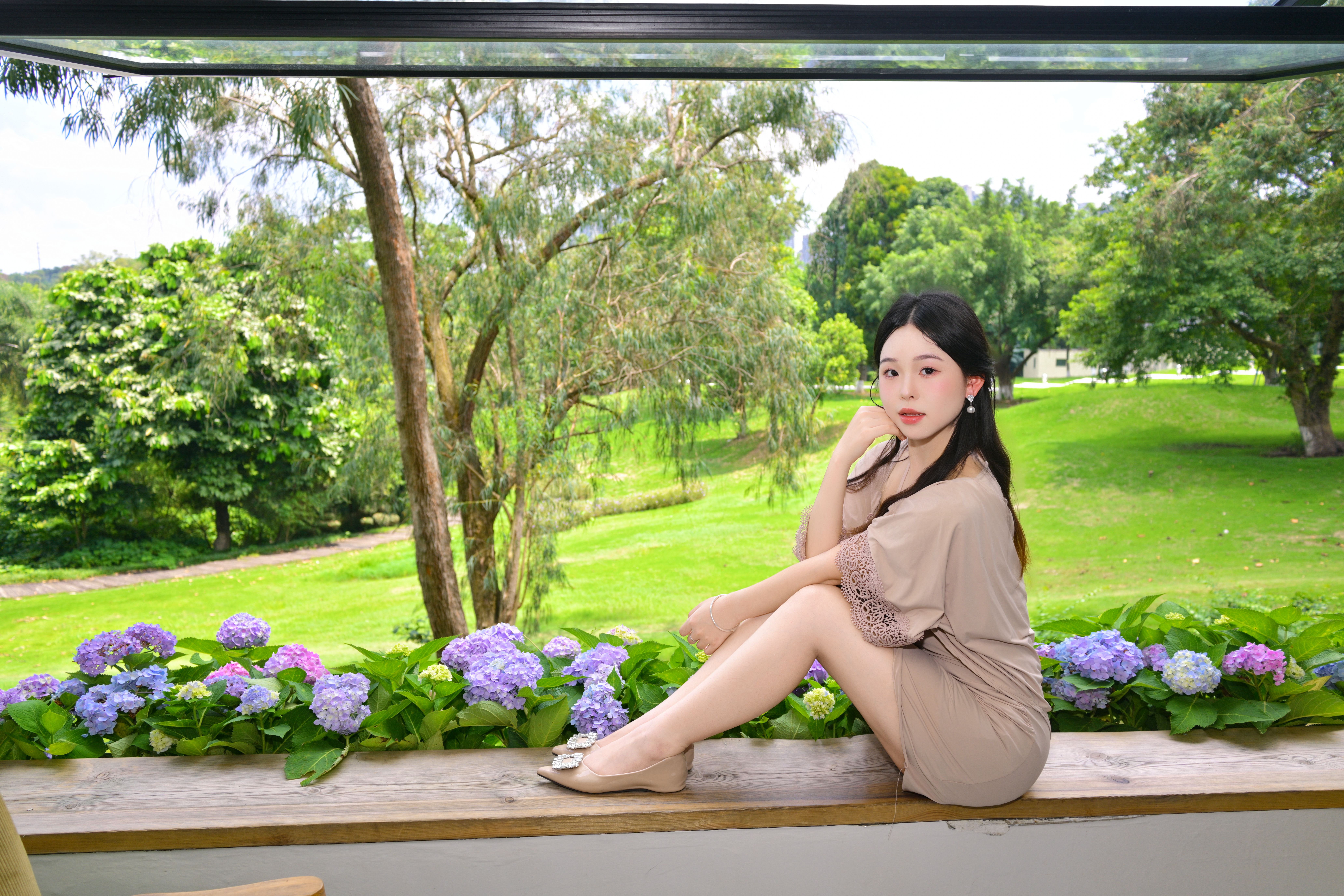 A young woman sitting on a ledge surrounded by hydrangeas, enjoying a sunny summer day.