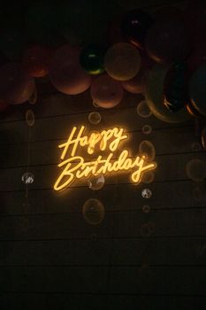 A vibrant neon 'Happy Birthday' sign surrounded by festive balloons.