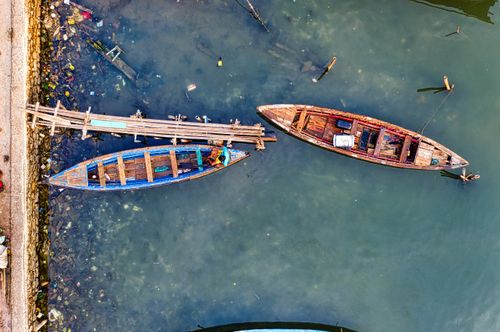 Free Aerial photo of wooden fishing boats tied to a rustic dock, showing clear water below. Stock Photo