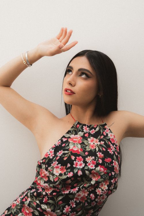 Free Elegant portrait of a woman posing in a floral dress with arms raised against a plain background. Stock Photo