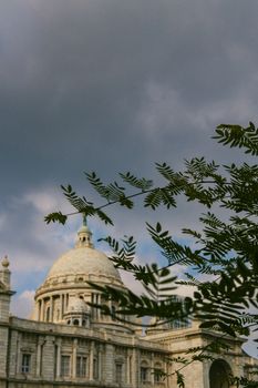 Victoria Memorial architecture framed by silhouetted leaves under a cloudy sky.