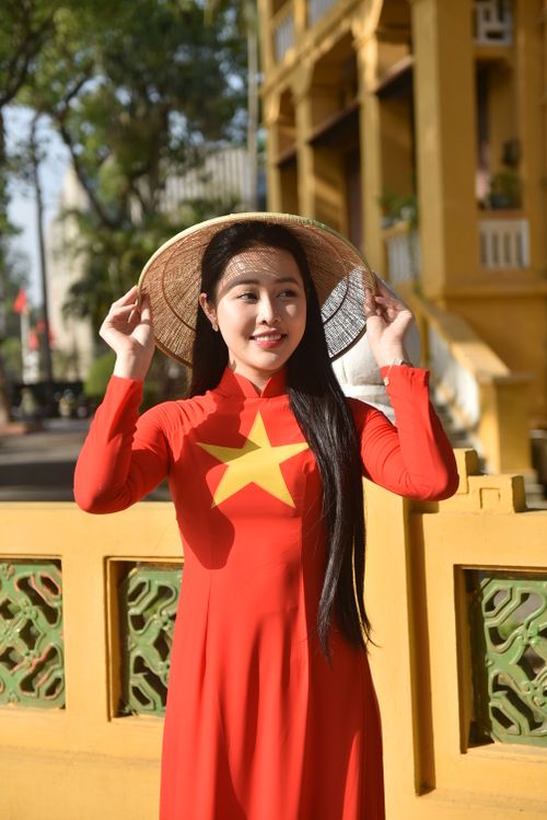 Free Young woman wearing red Ao Dai and conical hat smiling outdoors in vibrant setting. Stock Photo