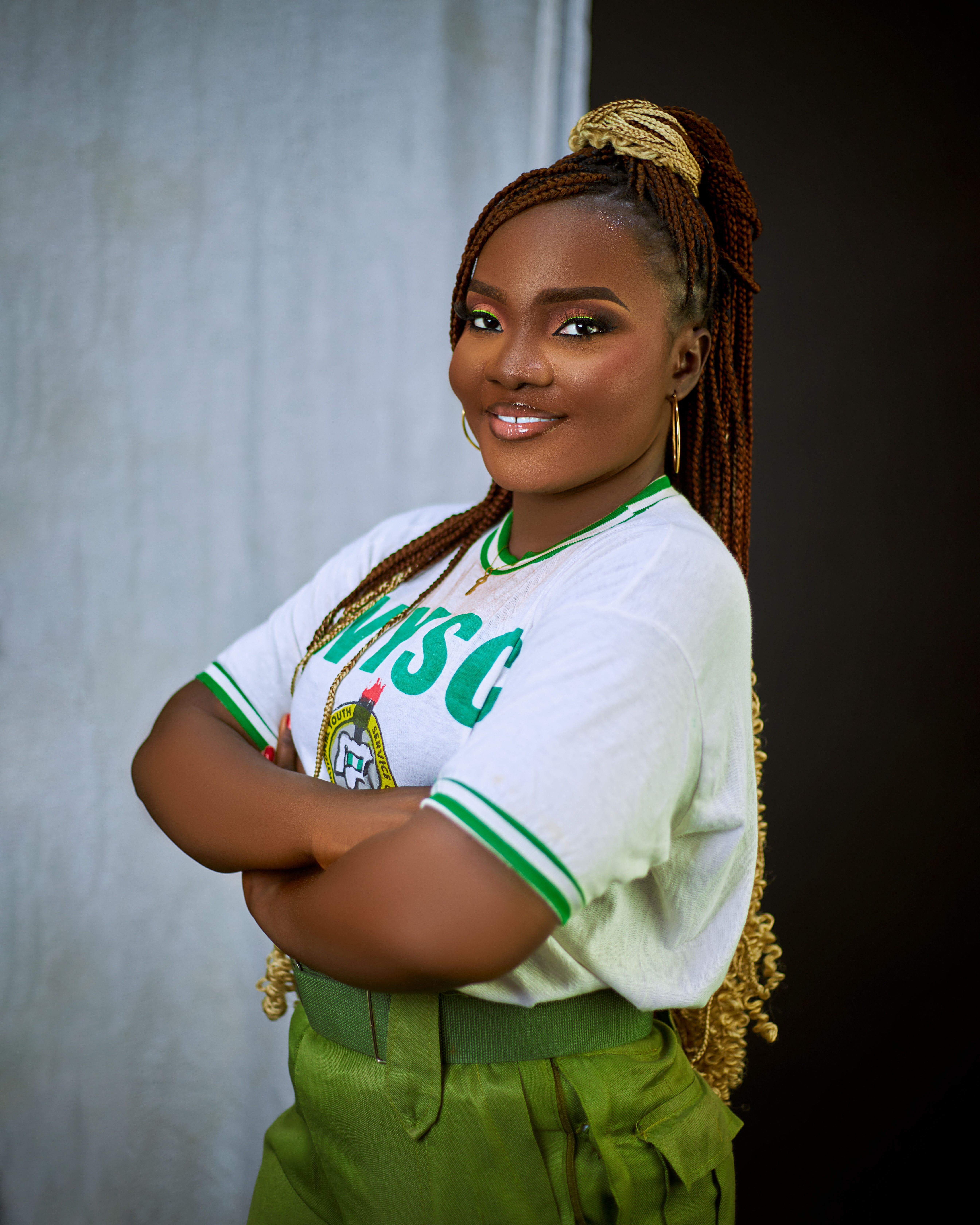 Smiling woman in NYSC uniform, arms crossed, confident pose