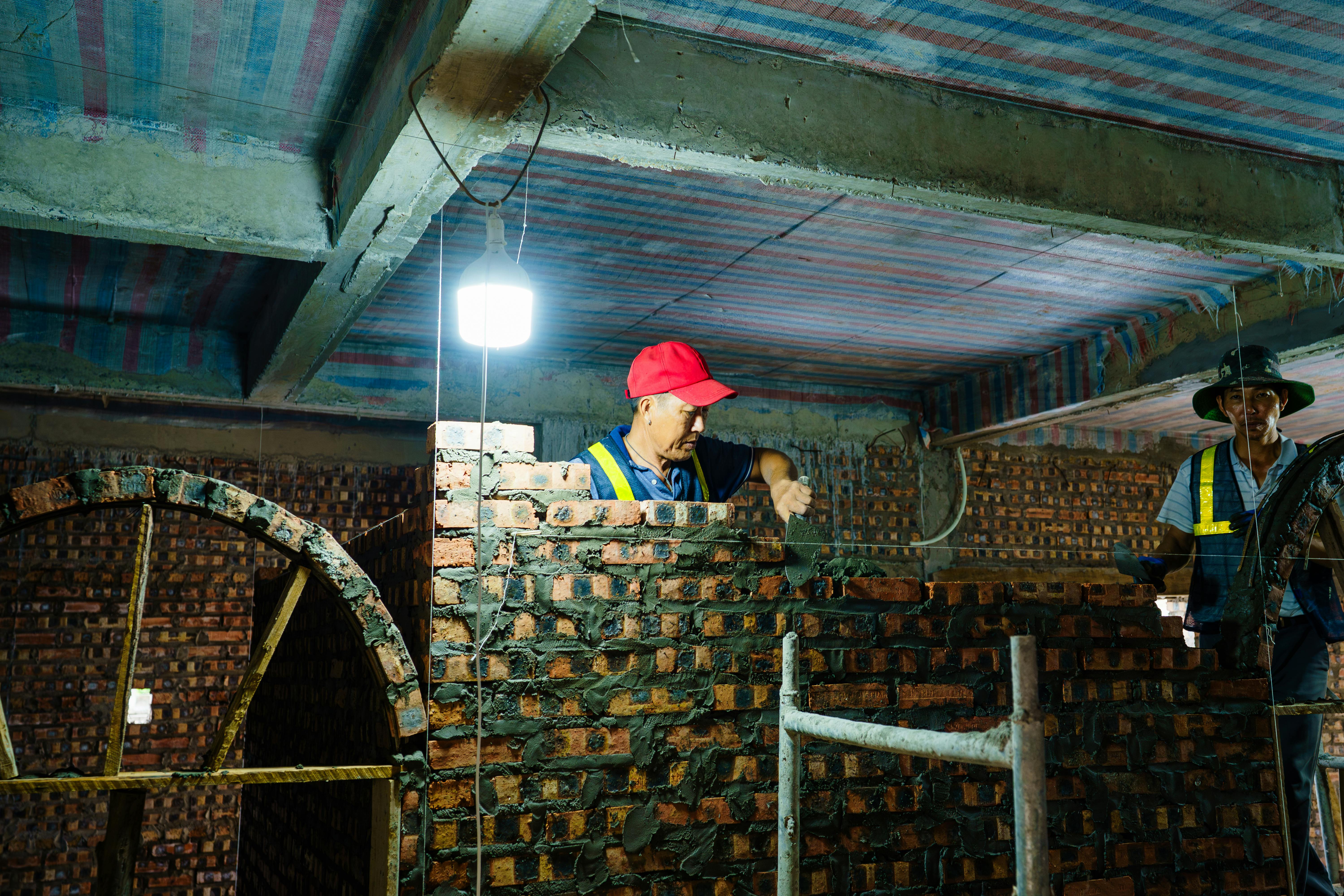 Des ouvriers construisent un mur de briques à l'intérieur dans un environnement faiblement éclairé à Hải Phòng, au Vietnam.