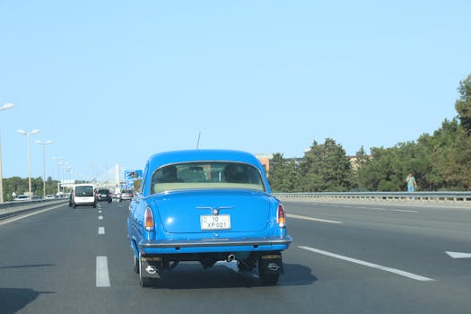 Classic blue car driving on a sunny highway, showcasing vintage design and open road travel.