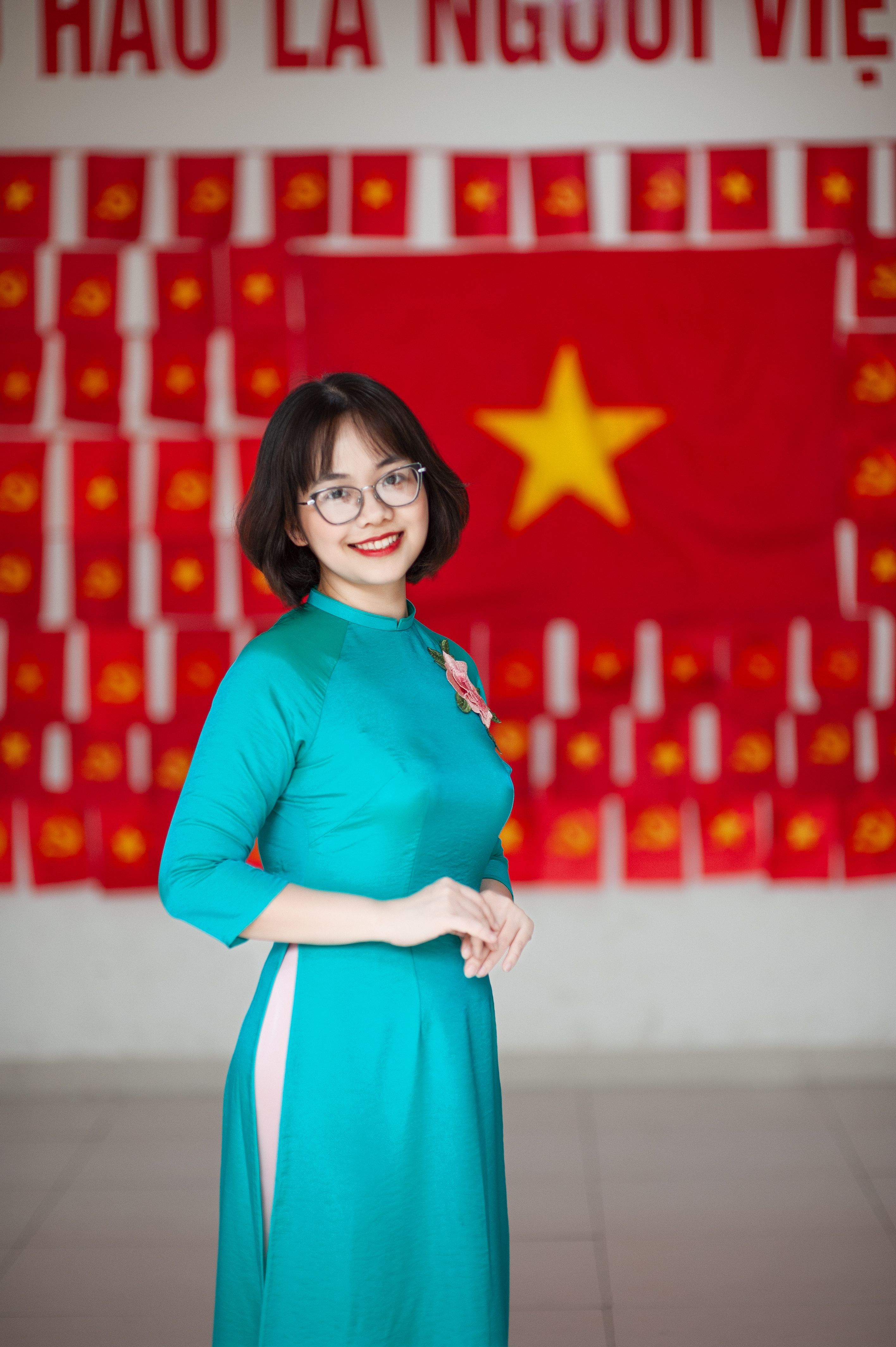 Portrait of a smiling young woman in traditional áo dài dress with Vietnamese flag background.