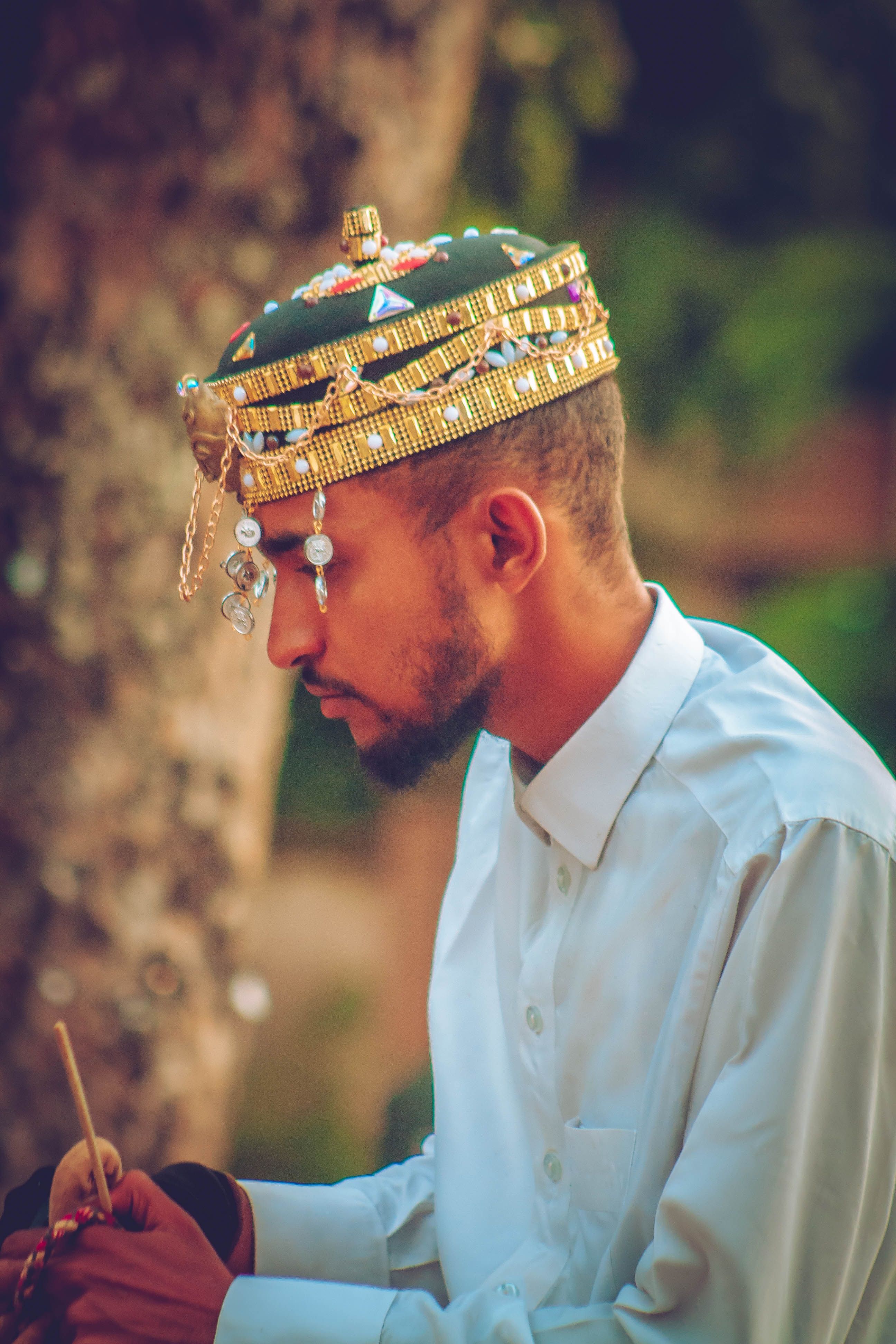 Profile of man in a white shirt wearing a traditional bejeweled cap outdoors.