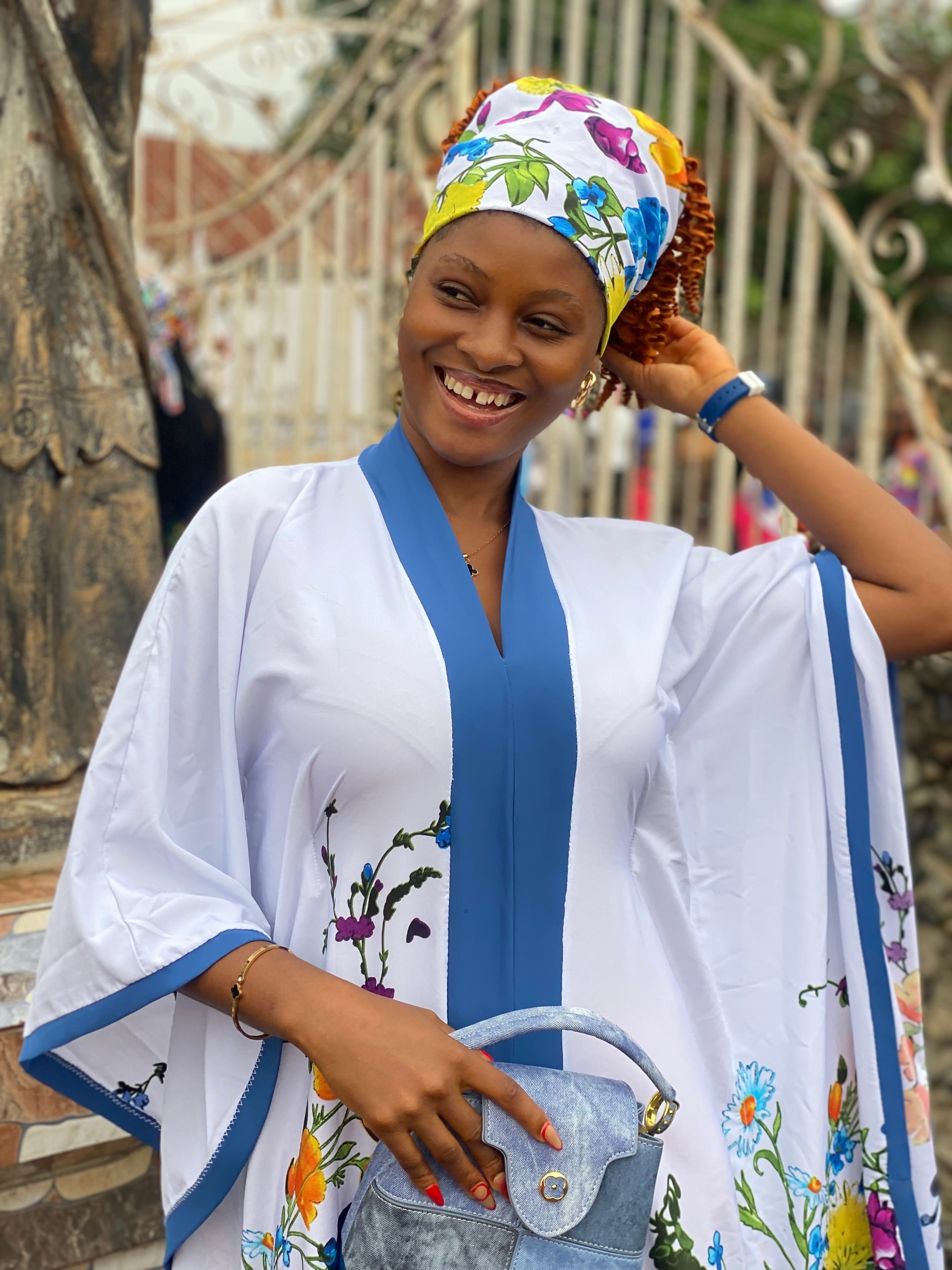 Joyful woman in a floral dress with headwrap, enjoying outdoors.