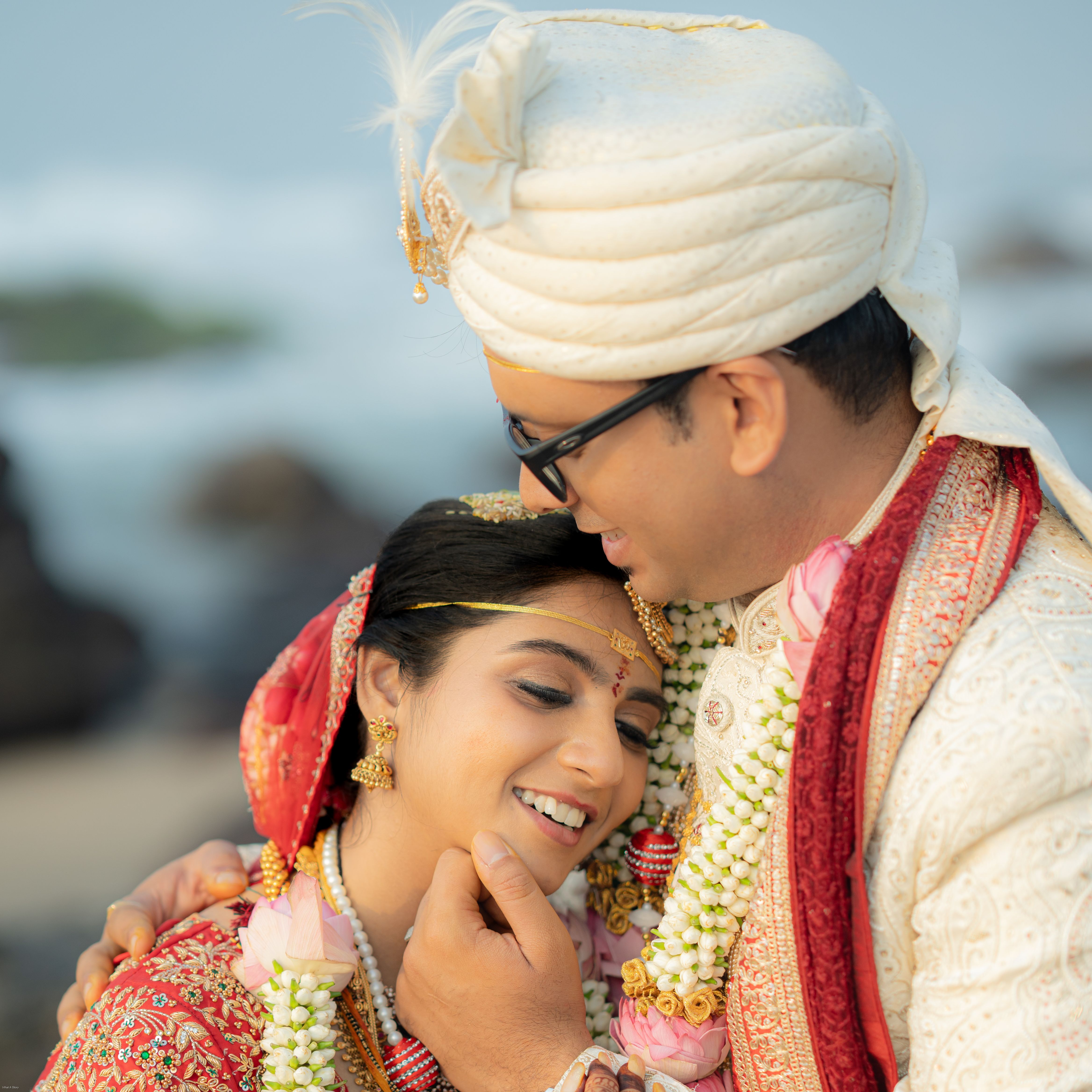 Beautiful Indian couple embracing in traditional wedding attire at a beachside ceremony.