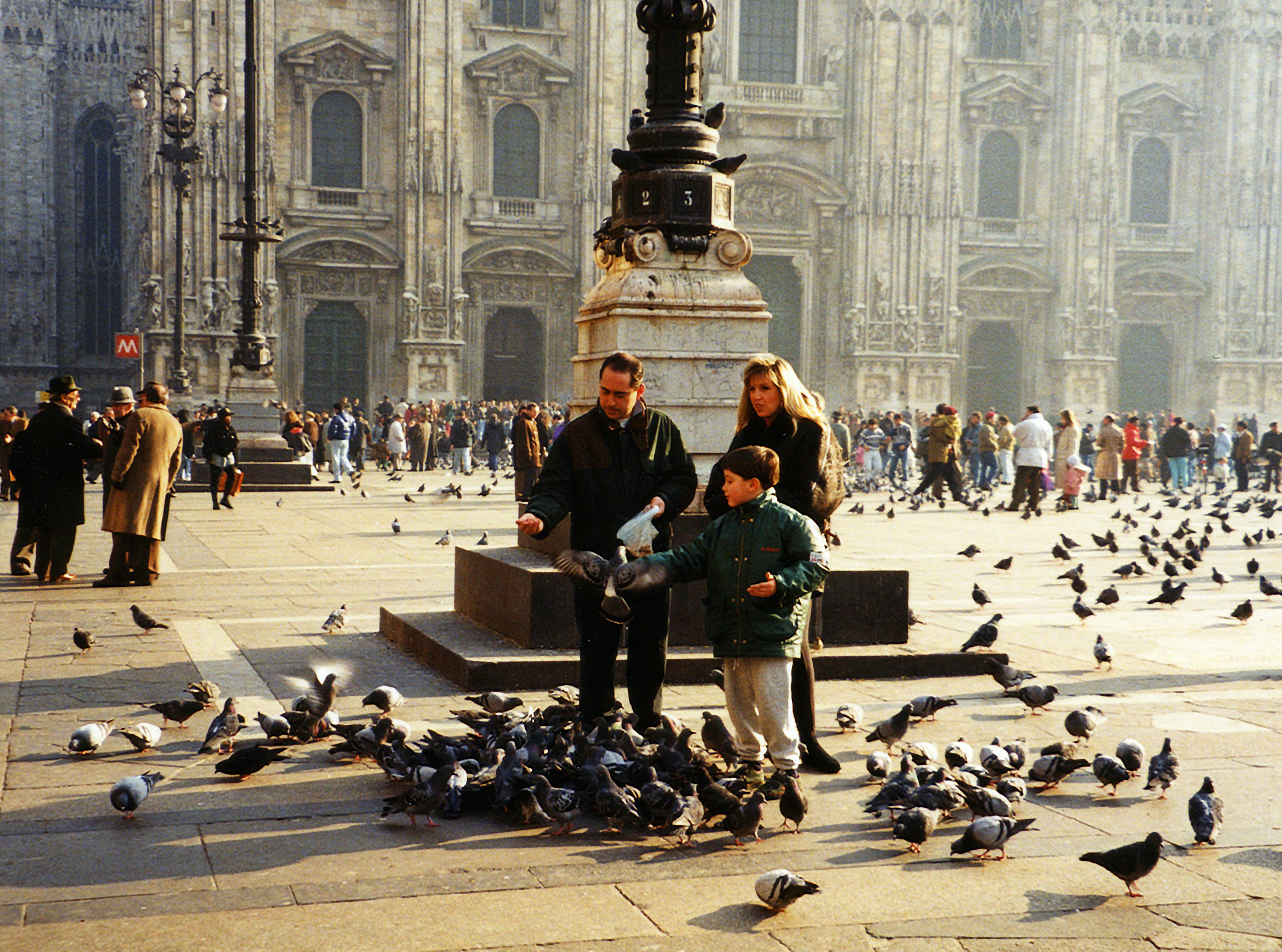 A family enjoys feeding pigeons at Piazza del Duomo, Milan, in front of the historic cathedral.