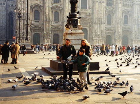 A family enjoys feeding pigeons at Piazza del Duomo, Milan, in front of the historic cathedral.